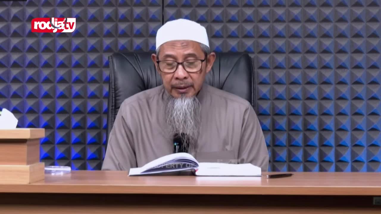 A man in a white peci and glasses reads from an open book. The Rodja TV logo appears in the upper left corner. A man in a white peci and glasses reads from an open book. The Rodja TV logo appears in the upper left corner.