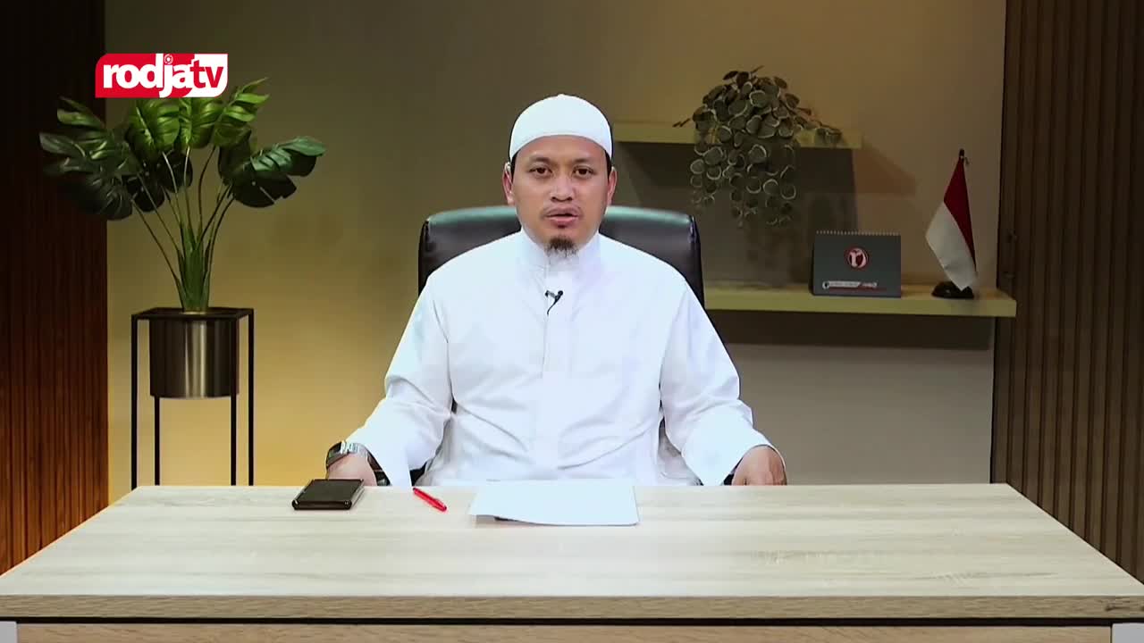 A man in a white peci and robe speaks into a microphone, seated at a desk. A Rodja TV logo is visible in the upper left corner, and an Indonesian flag stands on a shelf behind him.