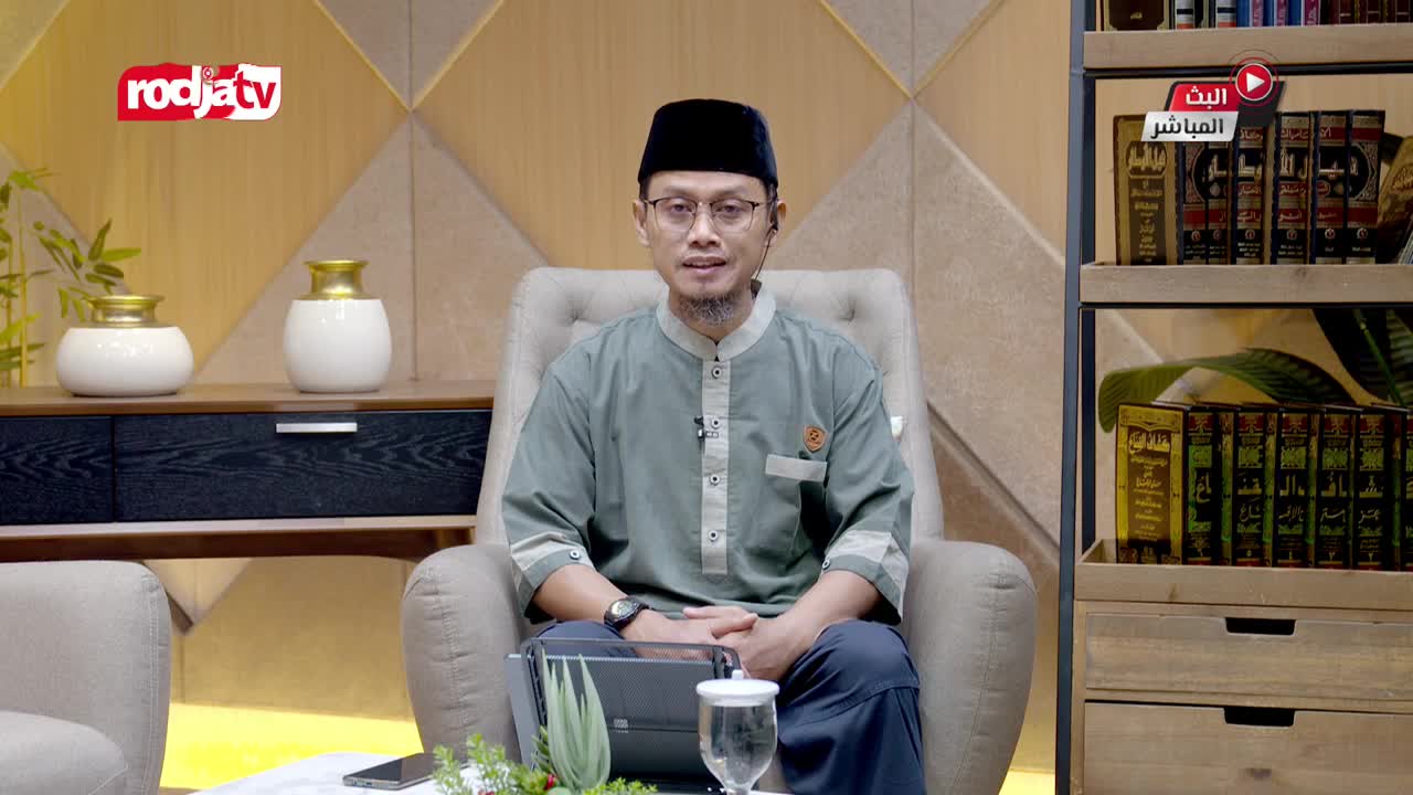 A man in a peci and a light green koko shirt sits in a plush chair, looking directly ahead. Behind him, a Rodja TV logo is visible, and a shelf displays rows of Islamic books.