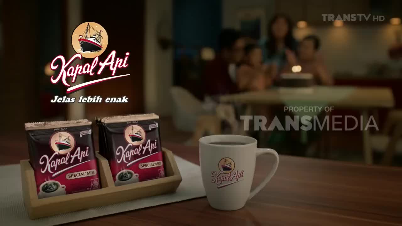 A mug of hot coffee and two packets of Kapal Api Special Mix sit on a wooden tray, with a family blurred in the background. The scene is part of a commercial on Trans TV in Indonesia.
