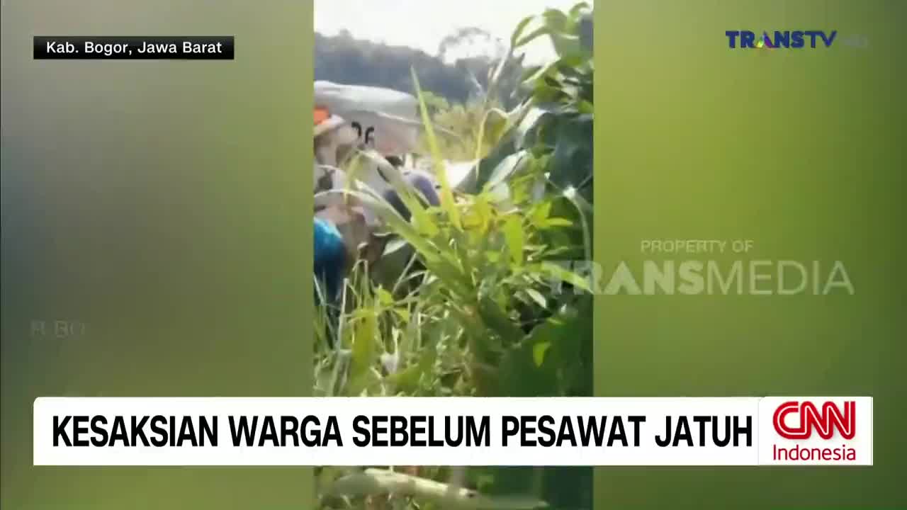 Through the tall grass, people are gathered near what looks like a plane. A Trans TV logo is visible, and the chyron indicates this is a report from Kab. Bogor, Jawa Barat, Indonesia.
