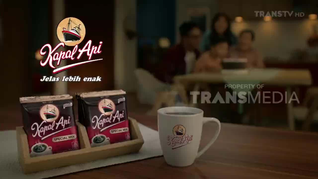 Two packets of Kapal Api coffee sit in a wooden tray, next to a mug filled with the dark beverage. In the background, a family is gathered around a table, likely watching Trans TV.
