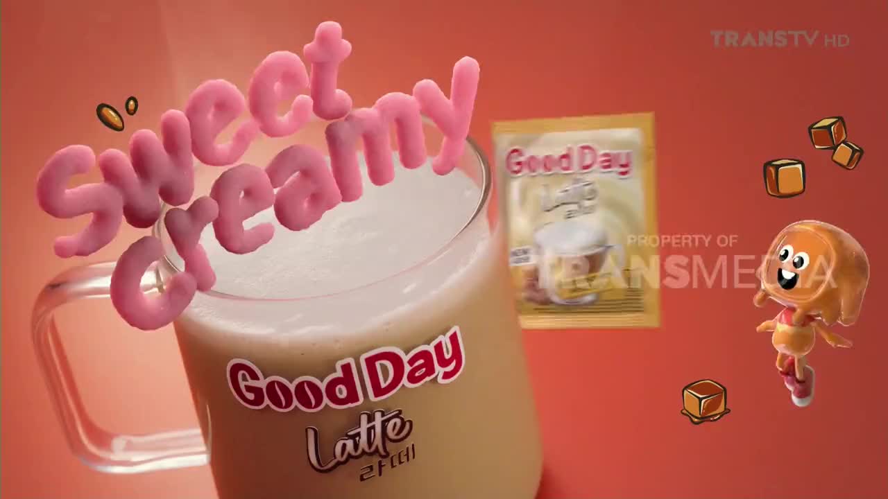 A mug of Good Day Latte sits with a frothy top, while the words "sweet creamy" float above it. A cartoon character and floating caramel cubes add to the scene, all against a backdrop of Trans TV branding.

