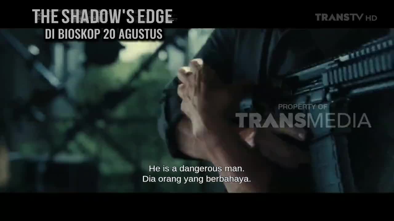A man grips a rifle, his arm muscles tense. The Indonesian channel Trans TV logo is visible, and a tagline warns that he's dangerous.
