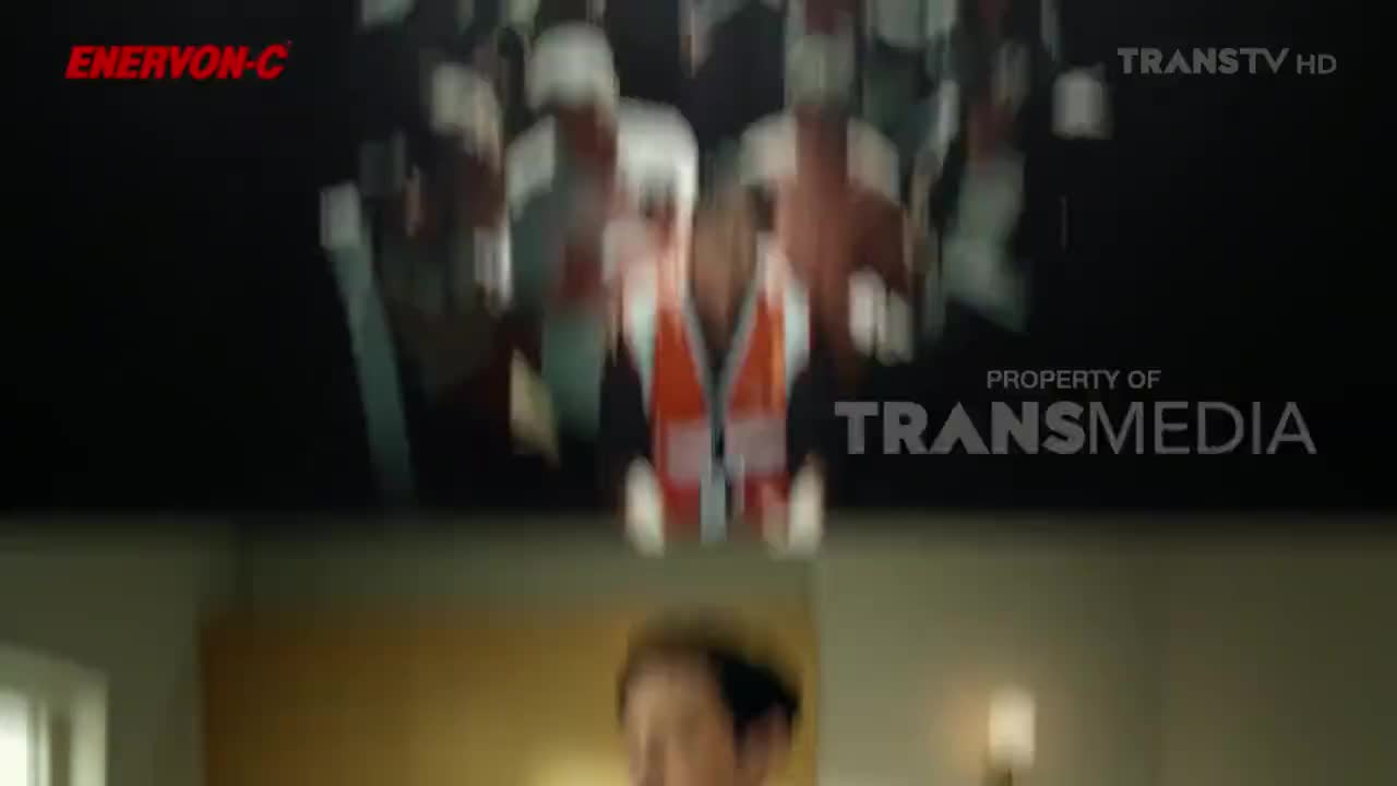 On the television screen, a person in an orange vest is barely visible, part of a scene on Trans TV. Below the screen, a person's face is visible, their expression unclear.
