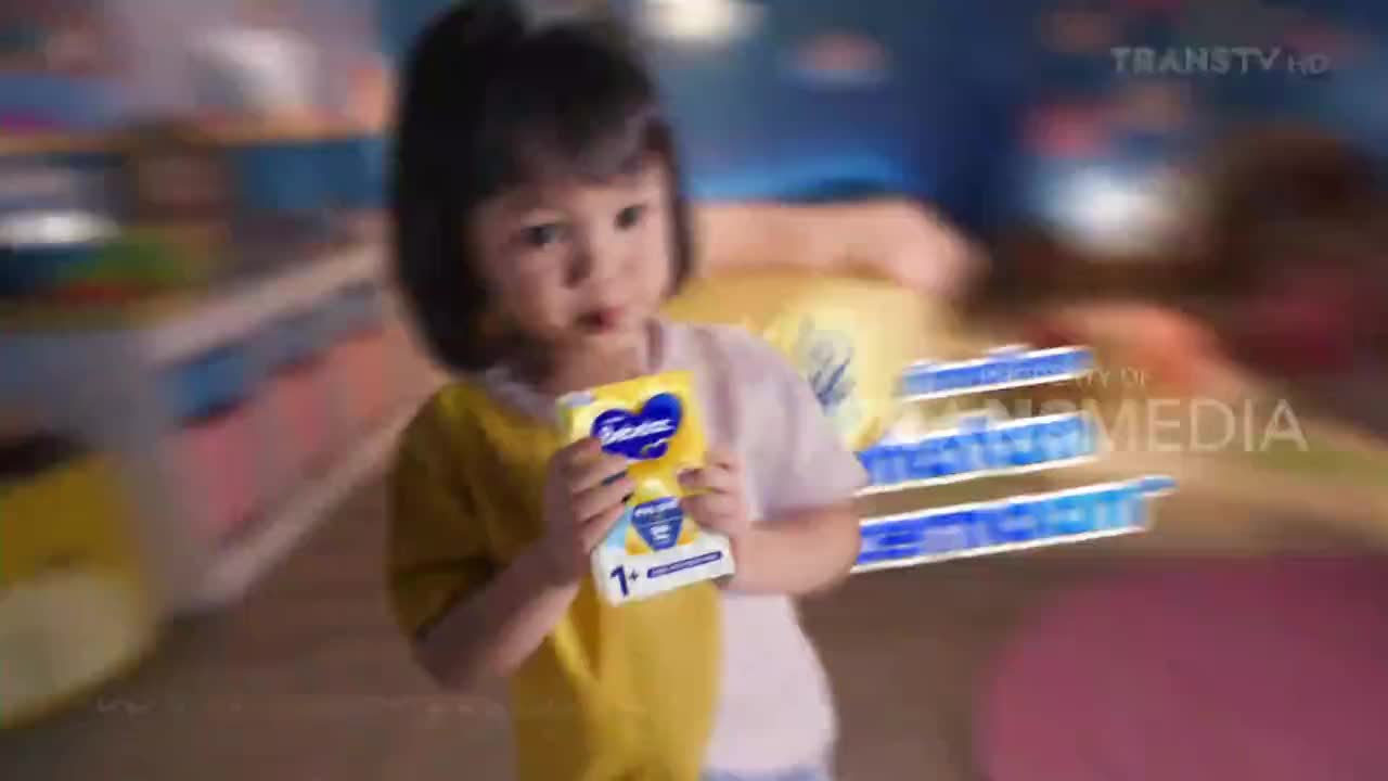 A young child, likely in Indonesia, holds a small box of formula, looking directly at the camera. The Trans TV logo is visible in the corner, suggesting this is a commercial or program segment.
