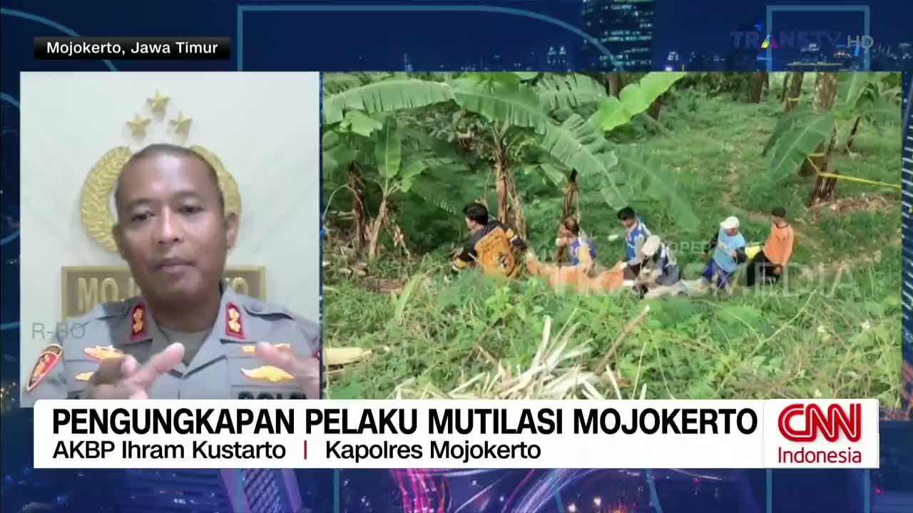 On Trans TV, a police officer in uniform is speaking, gesturing with his hands. In the background, a group of people are gathered in a grassy area, possibly at a crime scene in Mojokerto, Indonesia.
