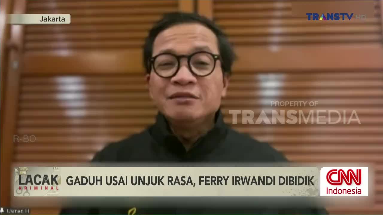 A man with glasses is speaking on Trans TV, framed against a wooden-paneled wall. The CNN Indonesia logo is visible, along with a headline about Ferry Irwandi.
