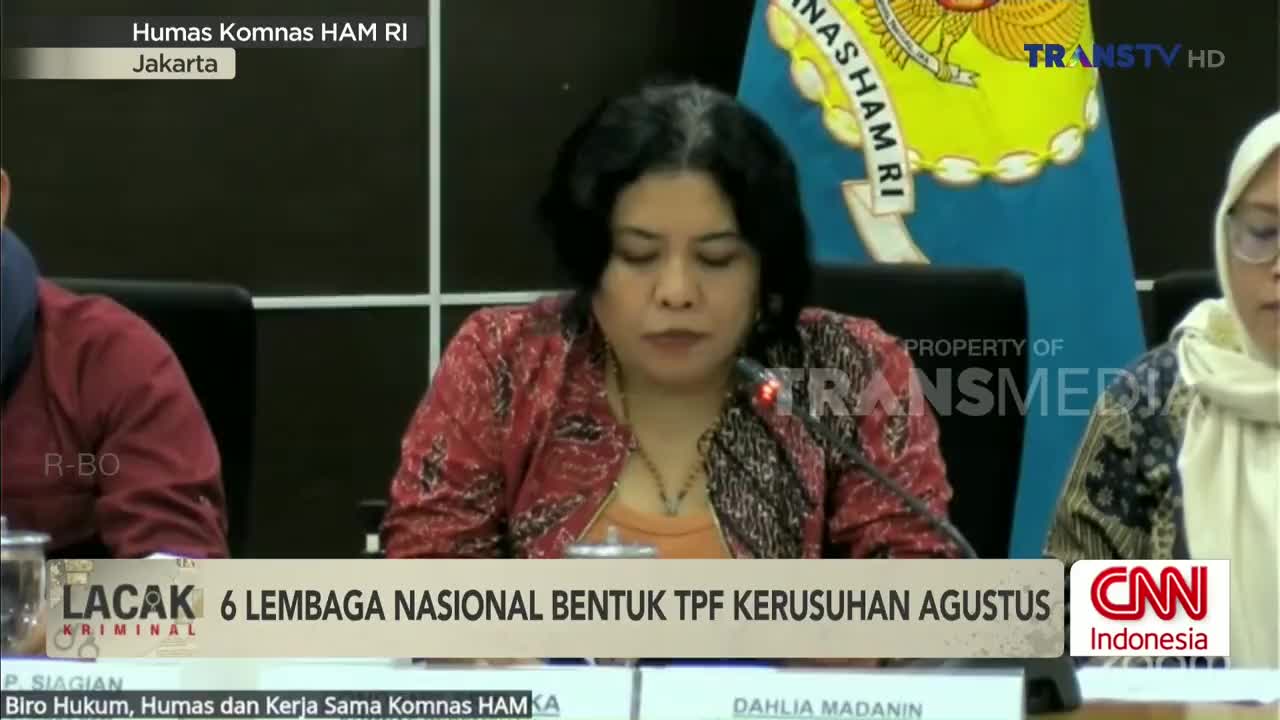 A woman in a patterned red jacket speaks at a table, a microphone positioned in front of her. The scene is being broadcast on Trans TV, with a CNN Indonesia logo visible in the corner.
