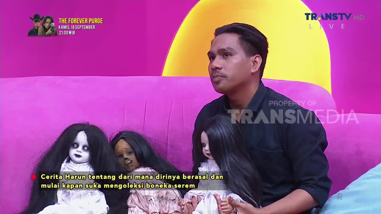 A man on the Trans TV set in Indonesia sits on a pink couch, flanked by several unsettling dolls. The caption below the dolls indicates a discussion about Harun's origins and his interest in collecting creepy dolls.
