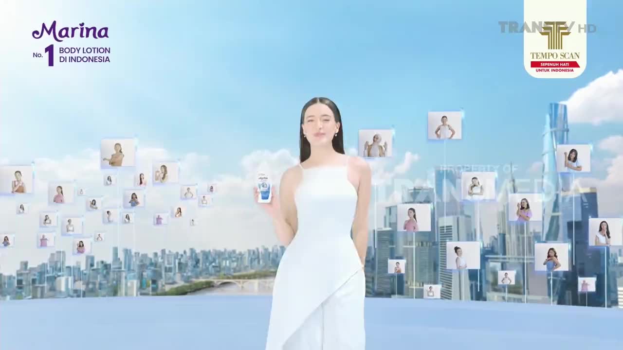 A woman in a white dress stands holding a body lotion bottle, facing the camera. Floating around her are small images of other women, all set against a backdrop of a city skyline and a bright blue sky, the Marina body lotion ad is on Trans TV.
