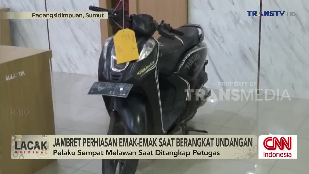 A black scooter with a yellow tag hangs in a room, likely a police station, as reported on Trans TV. The news segment from Indonesia discusses a jewelry theft.

