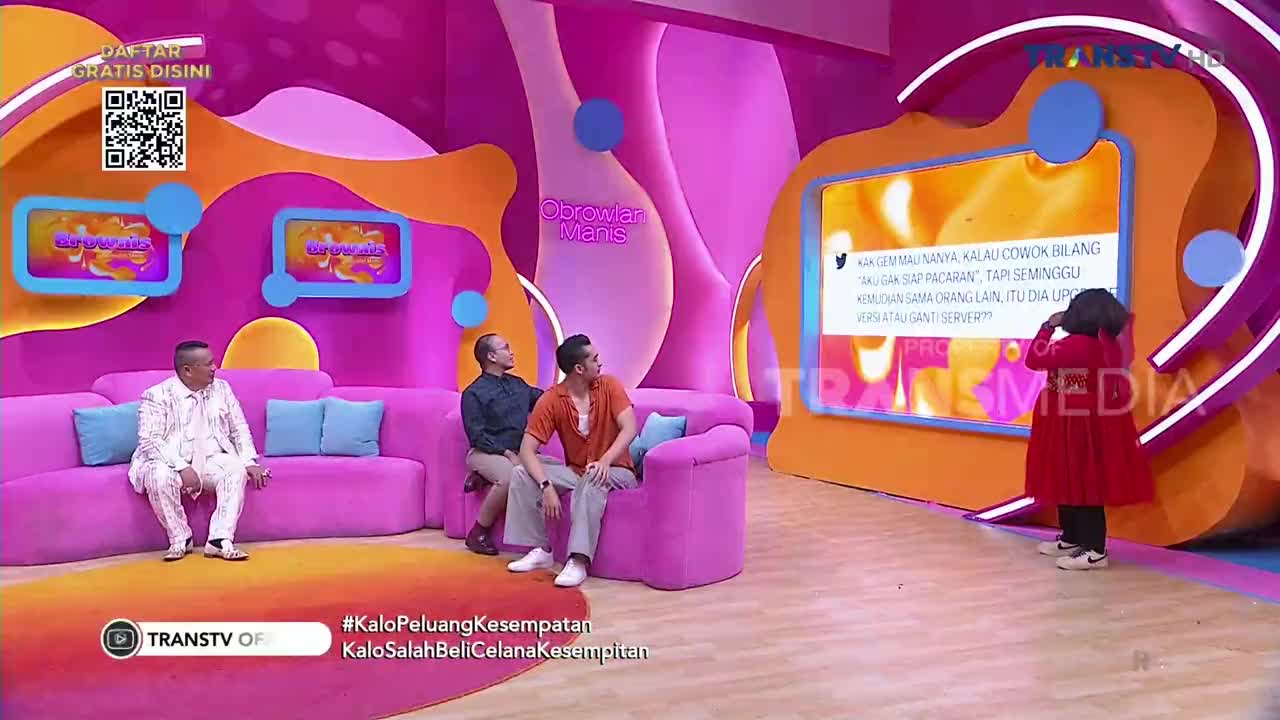 Three men sit on a pink couch on a Trans TV set in Indonesia, while a child in a red coat stands in front of a screen. The screen displays a tweet, and the child appears to be looking at it.
