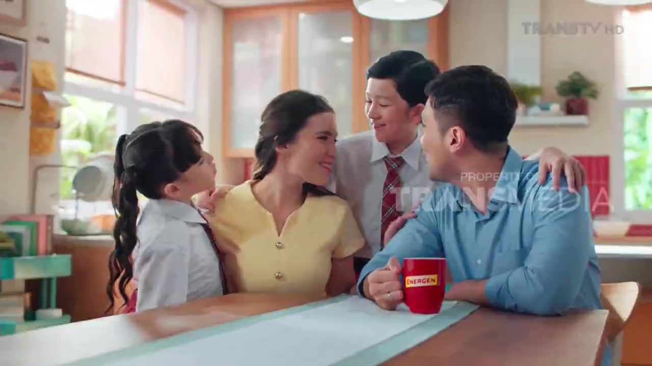 A family huddles together, smiling warmly around a kitchen table. The father holds a red mug, while the mother and children lean in close.
A family huddles together, smiling warmly around a kitchen table. The father holds a red mug, while the mother and children lean in close.