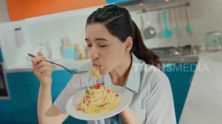 A woman, mid-bite, pulls a forkful of pasta from a plate, her eyes closed in enjoyment. The "Property of Transmedia" logo is visible, suggesting this is a cooking segment from Indonesian television.
A woman, mid-bite, pulls a forkful of pasta from a plate, her eyes closed in enjoyment. The "Property of Transmedia" logo is visible, suggesting this is a cooking segment from Indonesian television.