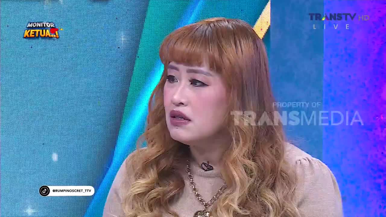 A woman with light brown hair and bangs speaks on a Trans TV show, her expression serious. The "MONITOR KETUA" graphic is visible on the left side of the screen.