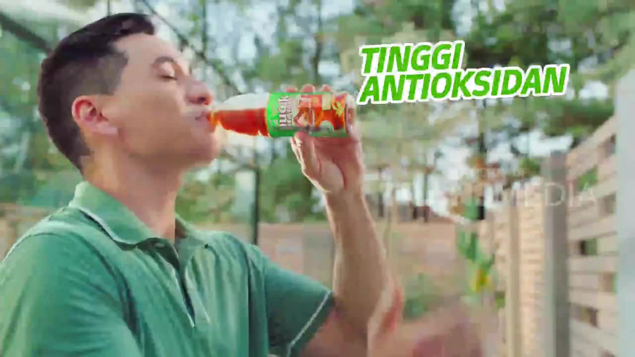A man in a green polo shirt drinks from a bottle of iced tea. The bright green text "TINGGI ANTIOKSIDAN" hovers over the scene.