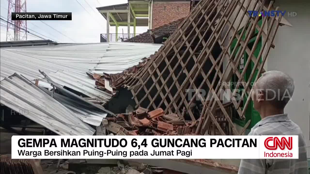 The roof of a building in Pacitan, East Java, has collapsed, with wooden beams and terracotta tiles scattered across the ground. An older man stands nearby, looking at the destruction.