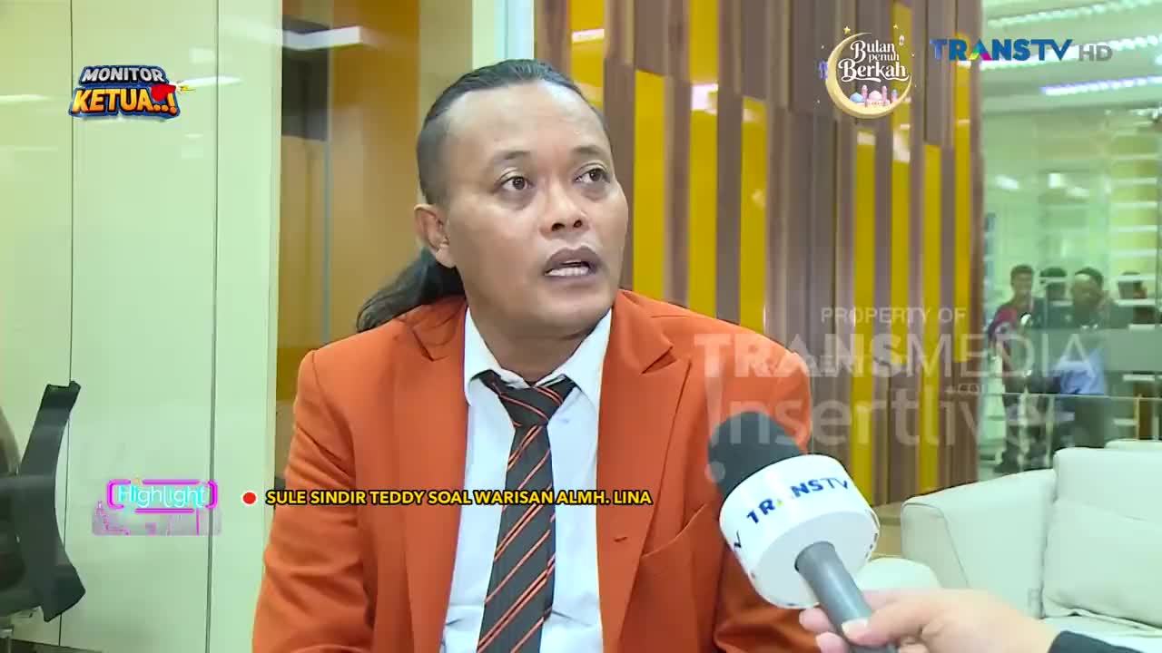 A man in an orange blazer speaks into a Trans TV microphone. The text on screen indicates he's discussing an inheritance.