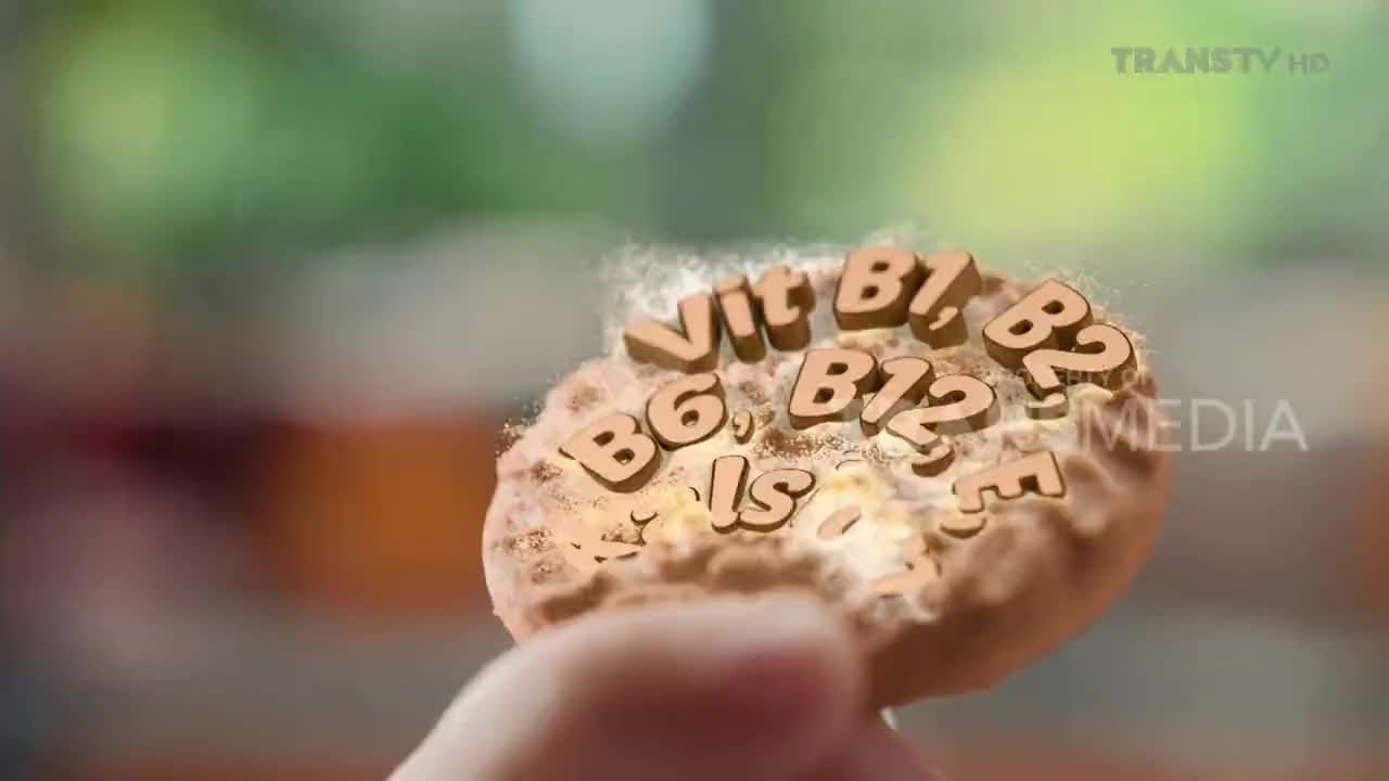 A hand holds a cookie, its surface embossed with wooden letters spelling out "Vit B1, B6, B12, B2, E." The Trans TV logo appears in the upper right corner.