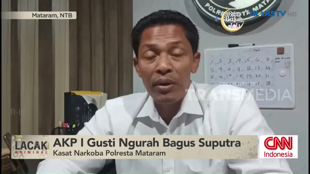 A man in a white shirt speaks directly to the camera, his voice clear. Behind him, a whiteboard displays a handwritten list of numbers. A logo for Trans TV is visible in the upper right corner.