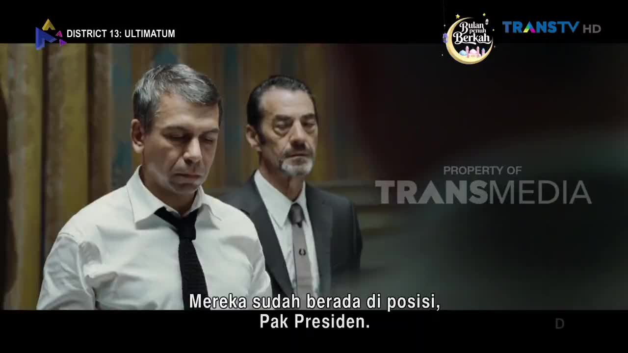 Two men in suits stand in front of a muted, textured wall, their gazes lowered. The Trans TV logo appears in the upper right corner, indicating this broadcast from Indonesia.