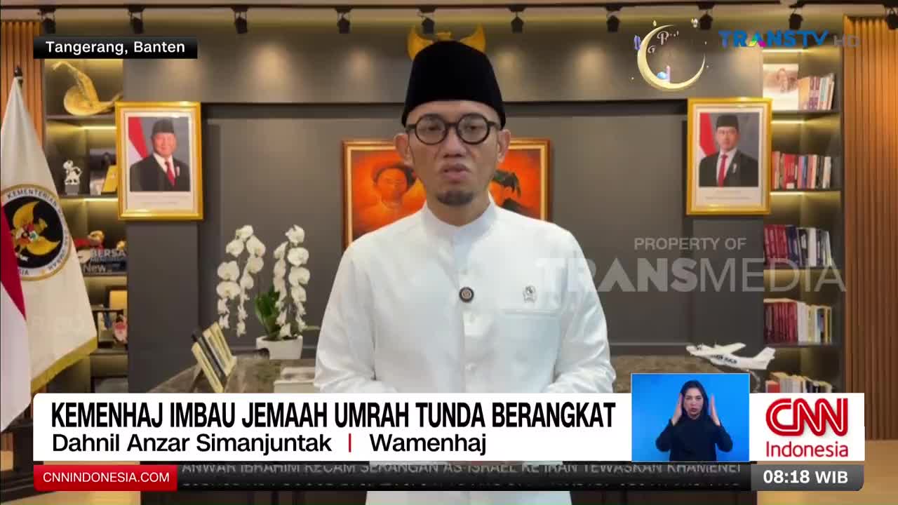 A man in a white shirt and peci speaks from a desk in Tangerang, Banten. A graphic overlay announces he is Dahnil Anzar Simanjuntak, Wamenhaj, and that the Ministry of Hajj is urging Umrah pilgrims to postpone their departure.