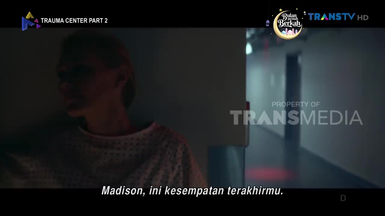 A woman in a hospital gown sits in a dimly lit room, her face obscured by shadow. The hallway behind her stretches into darkness, punctuated by faint red lights.