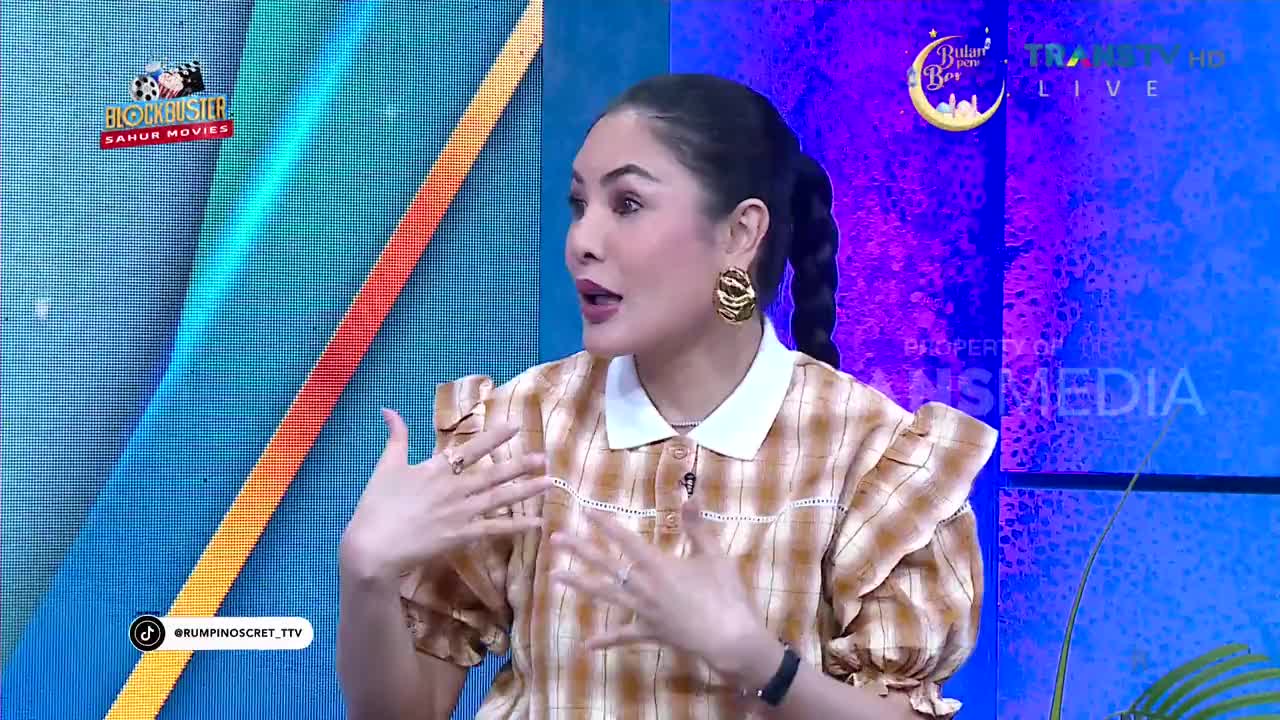 A woman with dark hair in a braid speaks animatedly, her hands gesturing. She's on a brightly lit set, likely for a Trans TV program in Indonesia.