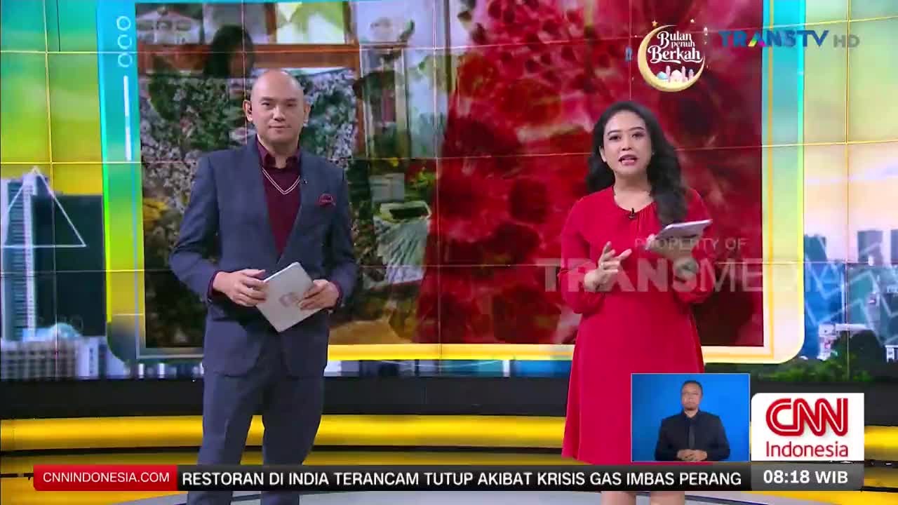 A man in a suit and a woman in a red dress stand on a brightly lit studio set, ready to present the news for Trans TV. Behind them, a large screen displays a graphic with the words "Bulan Penuh Berkah."