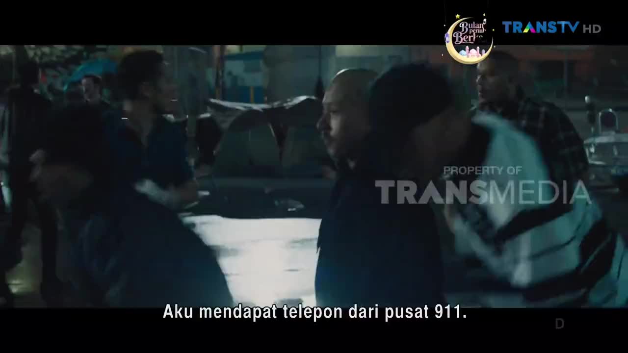 A crowd gathers, some people are jostling. A man with a shaved head turns his face towards the camera. The Trans TV logo is visible in the upper right corner.