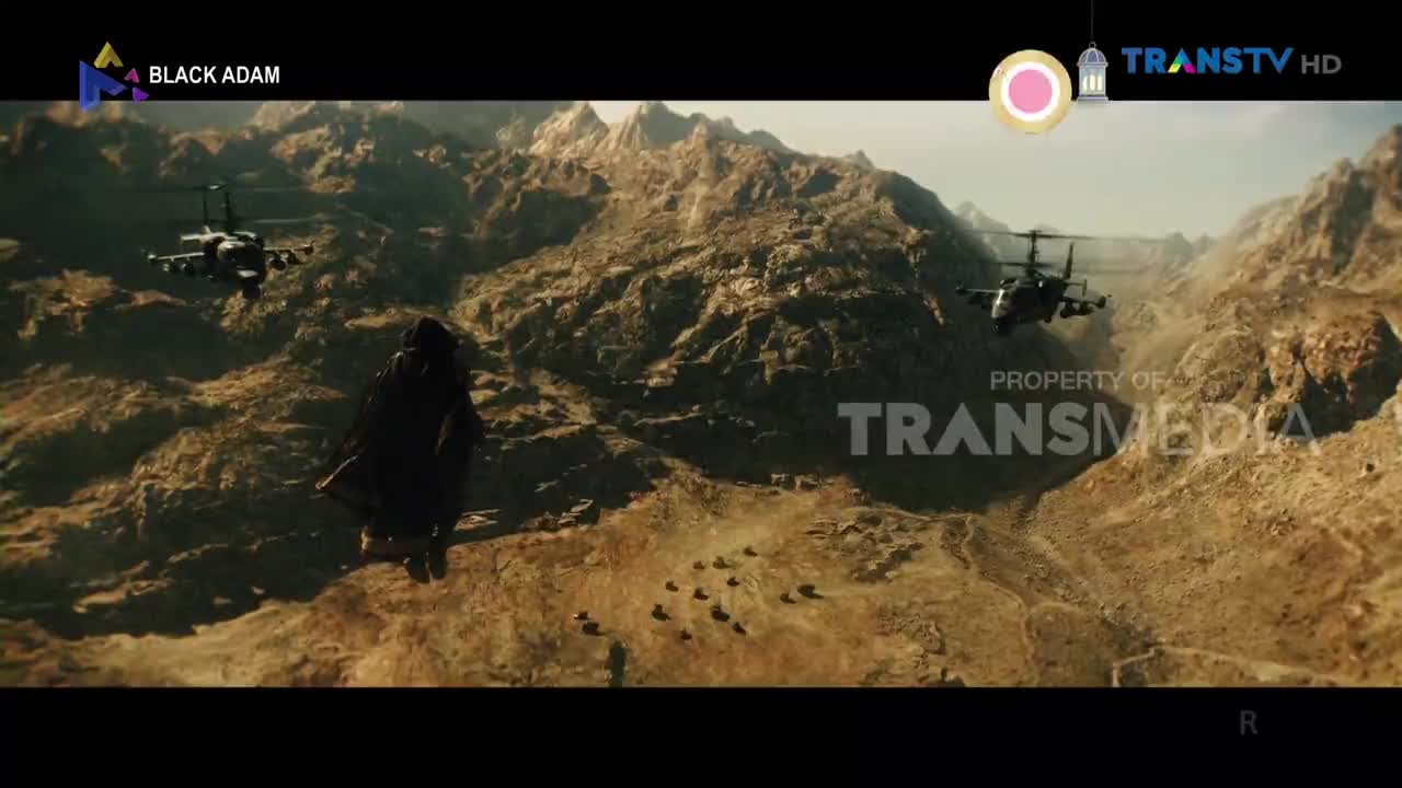 Two attack helicopters fly low over a rocky, desert canyon. A lone figure in dark robes stands facing them, silhouetted against the rugged landscape.