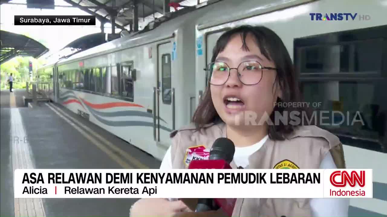 The train, with its distinctive orange and gray wavy stripes, is stopped at the Surabaya station. A young woman, holding a microphone for Trans TV, speaks animatedly about the Lebaran holiday travel.