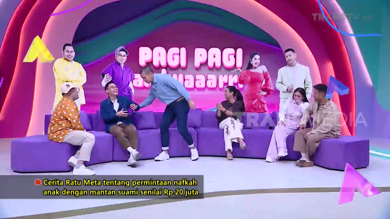 A man in a blue shirt leans over to touch the arm of a seated man in a blue jacket. The "Pagi Pagi Ambyar" logo glows behind them on the Trans TV set.