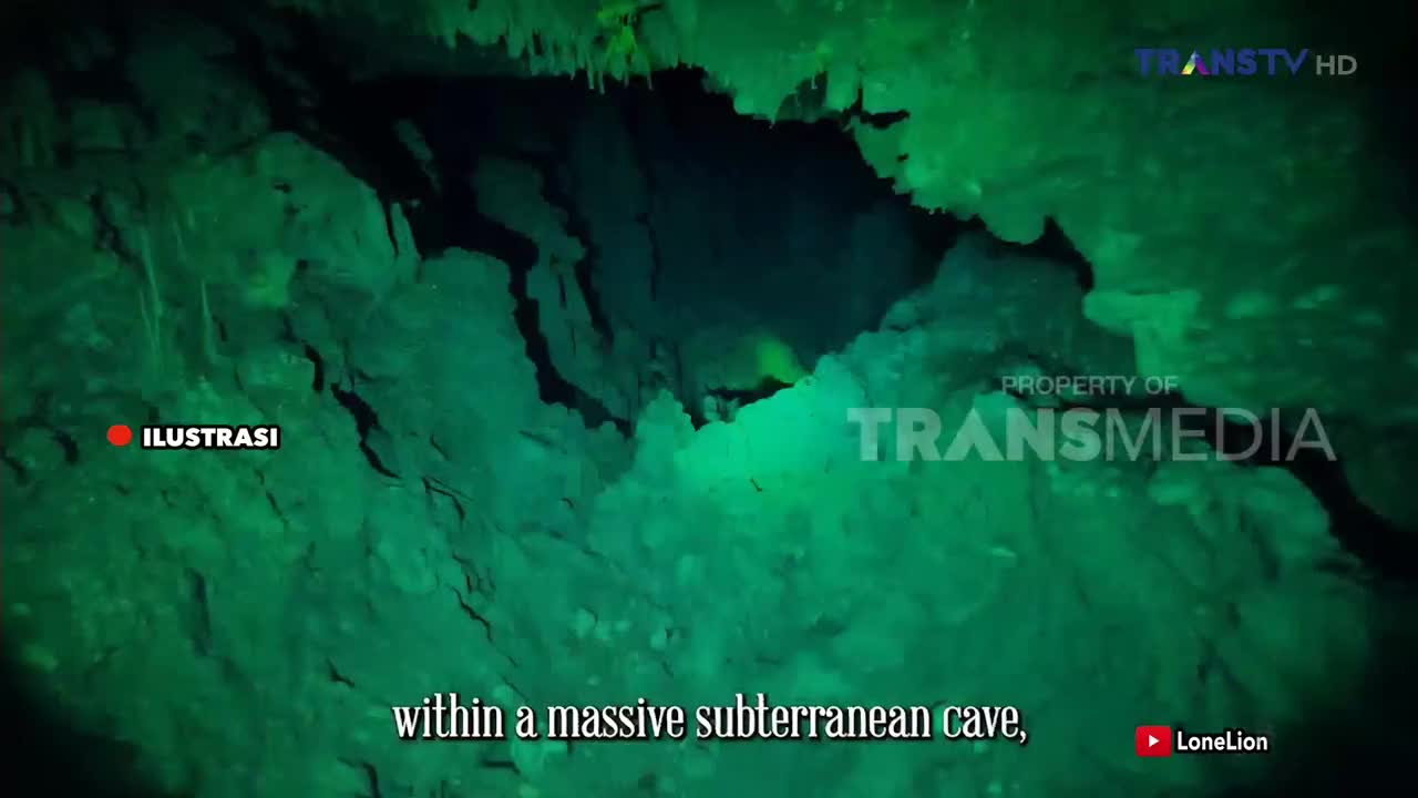 The camera glides through a vast, dark cave, illuminated by a green glow from the Trans TV broadcast. Jagged rock formations loom on either side, hinting at the immense scale of this subterranean space.