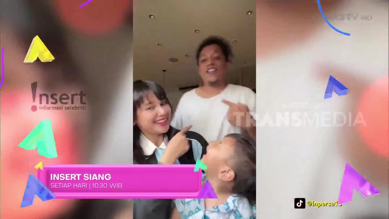 A woman in a white collared shirt playfully points at a child's open mouth, while a man behind them grins. The Trans TV logo appears on the right side of the screen.