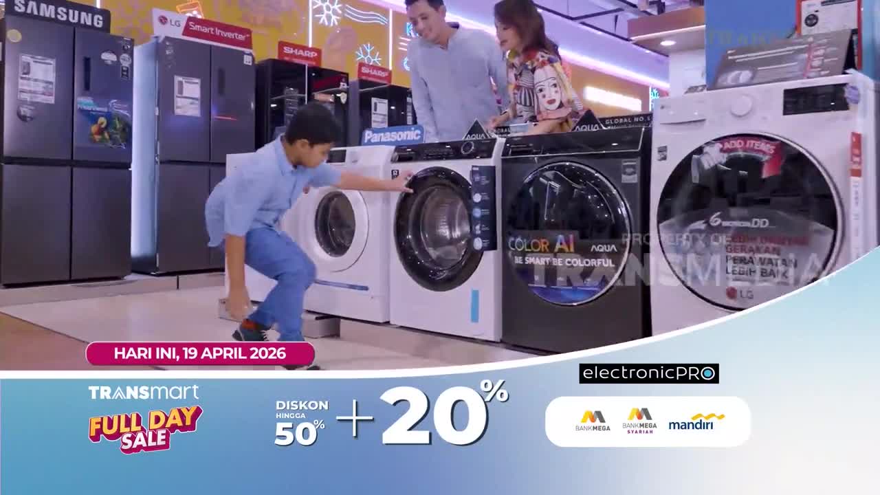 A young boy in a blue shirt crouches to examine a washing machine. A couple stands behind him, looking at the appliances on display.