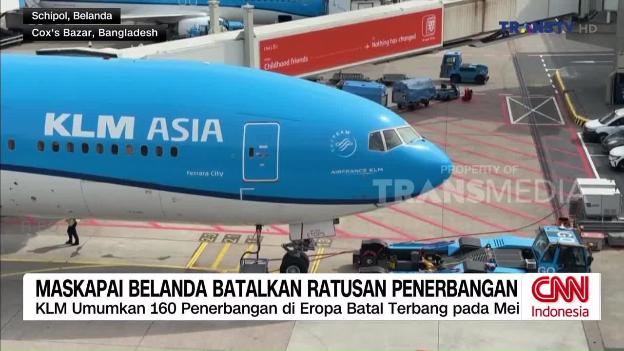A large KLM Asia airplane sits on the tarmac, its blue fuselage prominent. Ground crew and vehicles are positioned around the aircraft, suggesting preparations or maintenance.