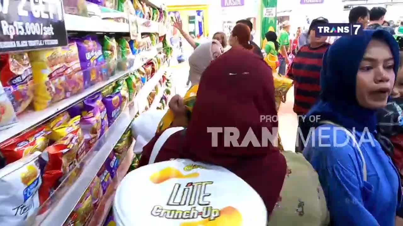 A woman in a maroon niqab is surrounded by other shoppers, with a "Lite Crunch-Up" container in the foreground. The scene is being filmed by Trans7 in what appears to be an Indonesian supermarket.

