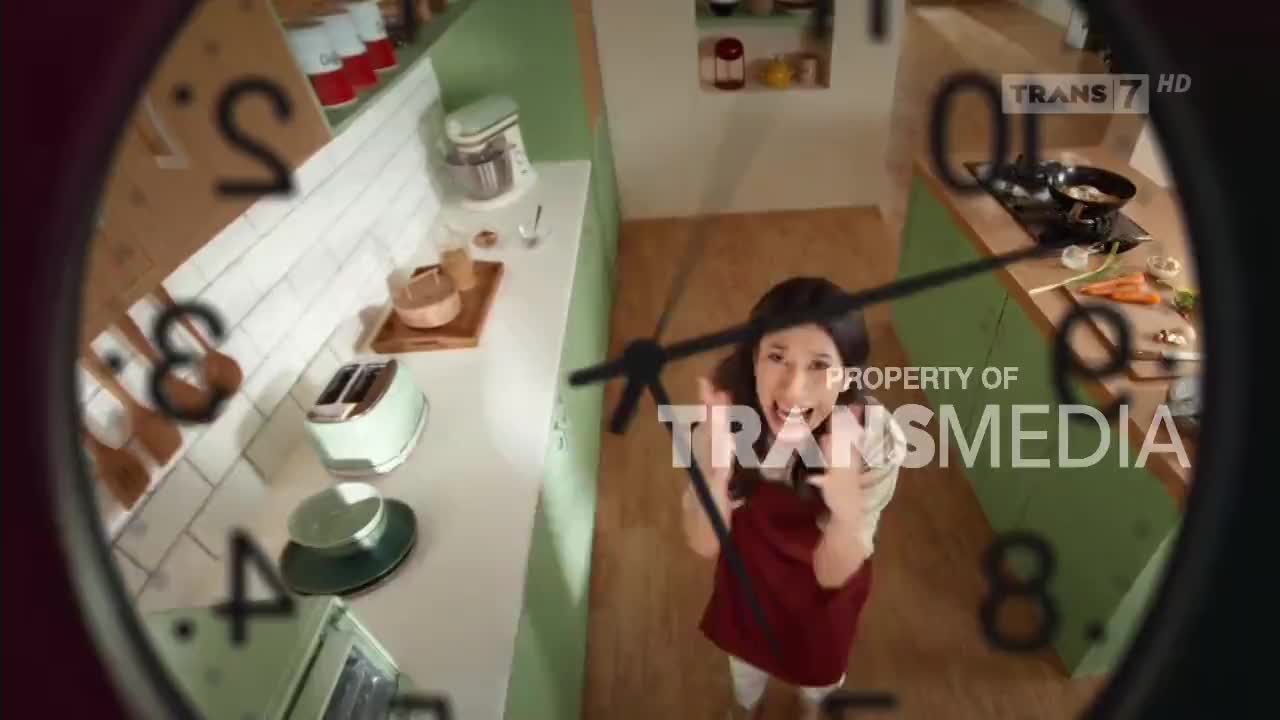 A woman in a maroon apron gestures excitedly in a kitchen, framed by a clock face. The "Trans7 HD" logo and "PROPERTY OF TRANSMEDIA" are visible, suggesting this is a cooking segment from Indonesia.
