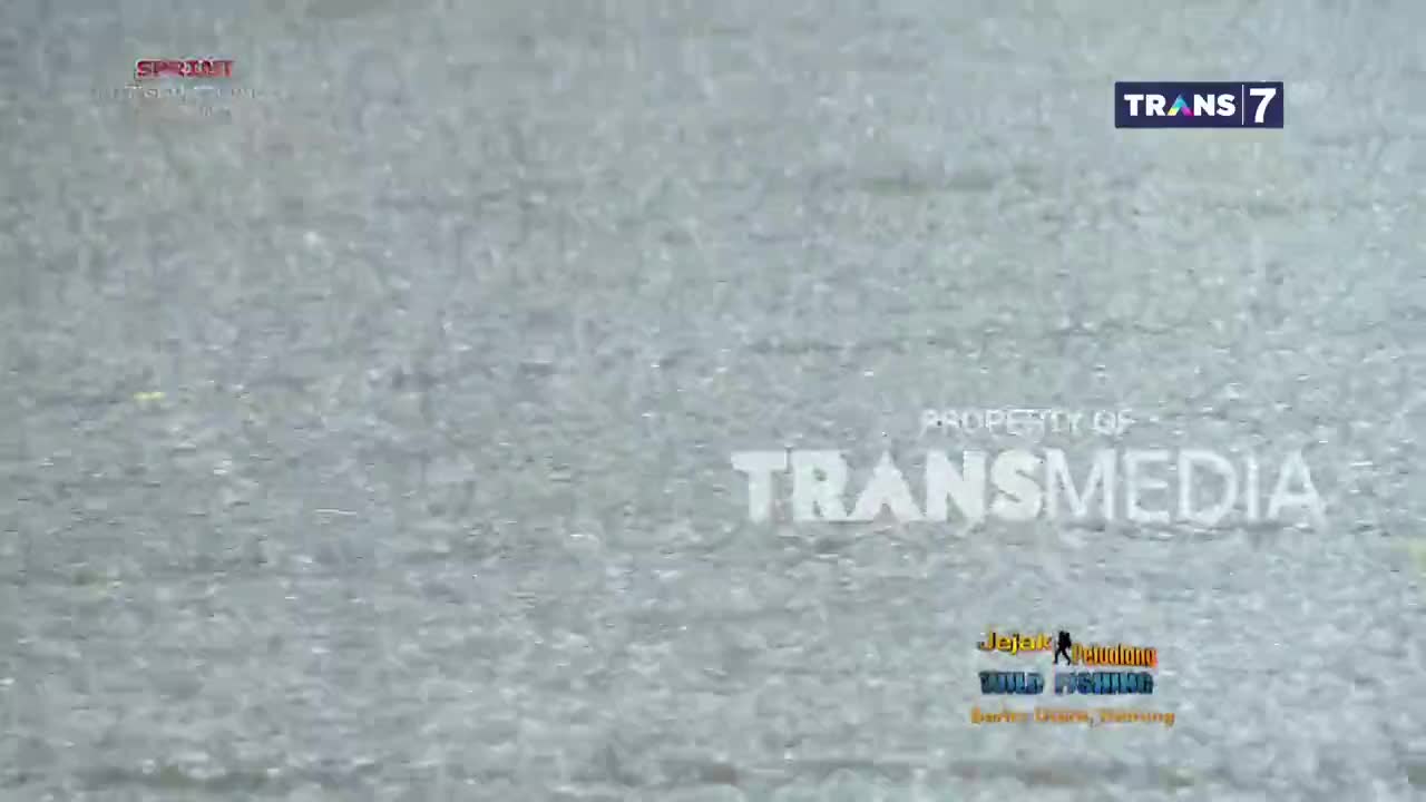 Raindrops are falling steadily, creating a textured, rippling effect across the screen. The Trans7 logo sits in the top right corner, while the Transmedia property notice and a fishing show logo are visible below.
