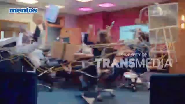 Furniture and papers are flying through the air inside an office, a chaotic scene. The "Property of Transmedia" logo is visible, suggesting this is part of a broadcast.
