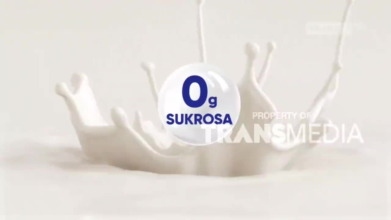 A splash of white liquid, like milk, forms a crown shape, with droplets reaching upwards. Floating in the middle, a blue circle on the Trans7 screen highlights "0g Sukrosa."
