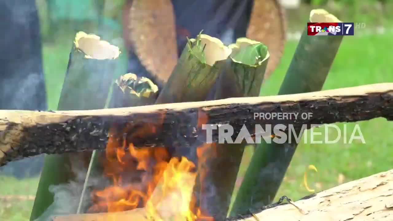 Flames lick at the charred wood supporting bamboo tubes filled with something cooking. The scene is being broadcast on Trans7, a channel from Indonesia.
