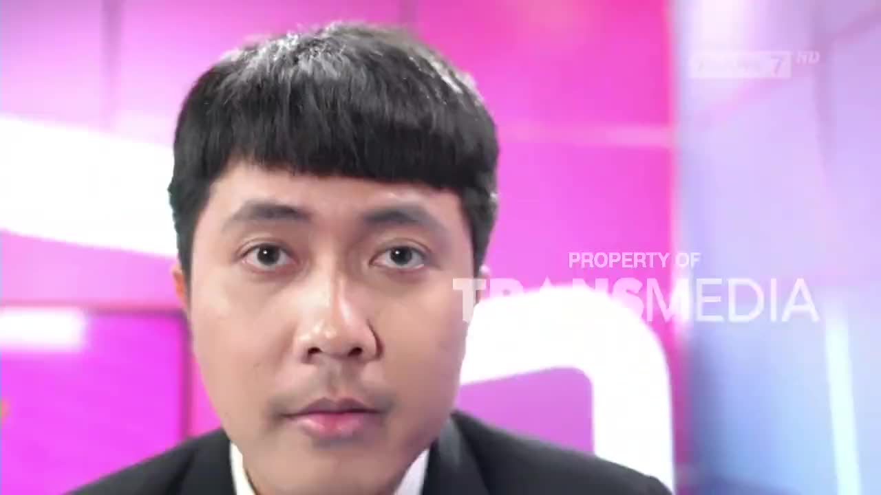 A man with a neatly trimmed bowl cut stares directly at the camera, his expression serious. Behind him, the Trans7 logo and a pink and purple backdrop suggest a studio setting in Indonesia.
