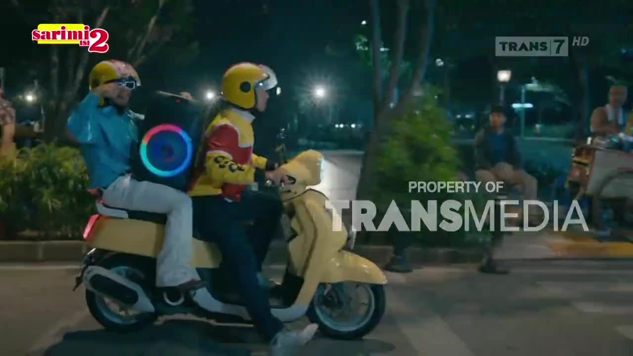 A yellow scooter with two riders speeds down the street, a glowing speaker strapped to the back. The scene is likely from a Trans7 show, judging by the logo.
