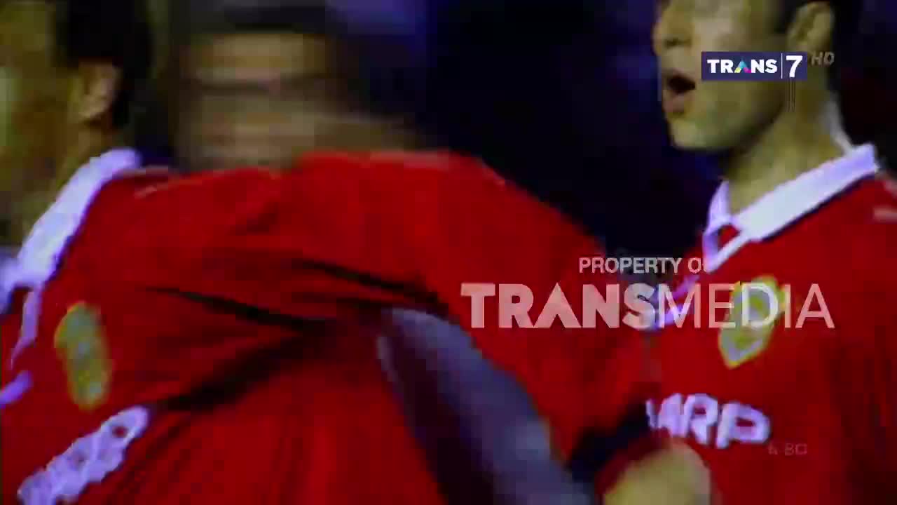 Two players in red jerseys are close together, one with his arm raised. The Trans7 logo is visible in the corner, broadcasting the game in Indonesia.
