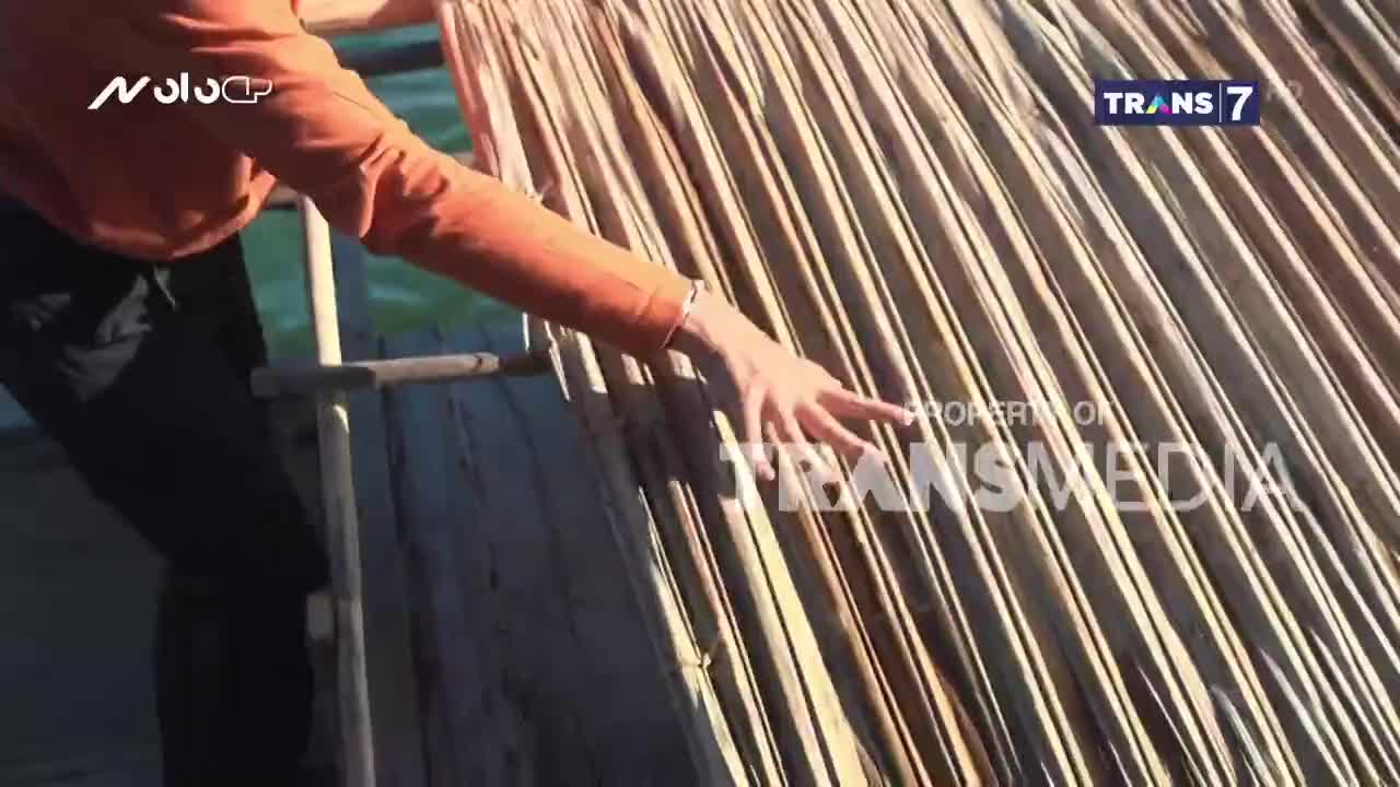 An arm in an orange shirt gently guides a hand across a woven surface, likely thatch. The Trans7 logo is visible, suggesting this is part of a broadcast from Indonesia.
