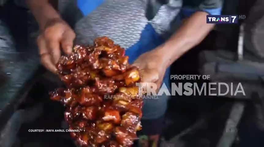 A cook holds a large portion of glistening, dark-red food, likely a dish from Indonesia, on display for the camera. The Trans7 logo is visible, indicating this is part of a broadcast.
A cook holds a large portion of glistening, dark-red food, likely a dish from Indonesia, on display for the camera. The Trans7 logo is visible, indicating this is part of a broadcast.