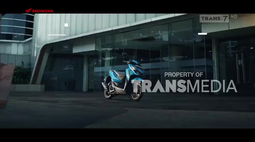 A sleek, blue scooter is parked in front of a modern building, its silver exhaust pipe glinting in the light. The Trans7 logo and "Property of Transmedia" are prominently displayed, suggesting this is a promotional shot for Indonesian television.
A sleek, blue scooter is parked in front of a modern building, its silver exhaust pipe glinting in the light. The Trans7 logo and "Property of Transmedia" are prominently displayed, suggesting this is a promotional shot for Indonesian television.